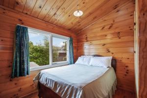 1 dormitorio con 1 cama en una habitación de madera con ventana en Lakefront Lodge - Kuratau Holiday Home en Kuratau