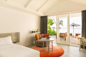 a bedroom with a bed and a table with a chair at LUX* South Ari Atoll Resort & Villas in Maamigili