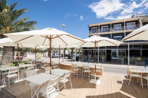 a patio with tables and umbrellas in front of a building at Hôtel Café Miramar in Le Grau-du-Roi