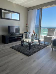 a living room with a television and a couch and a table at Infinity Self Catering Beachfront Apartment 302 in Cape Town +30 photos