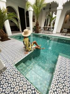 a child wearing a hat sitting next to a swimming pool at Riad Fabiola Et Spa in Marrakesh