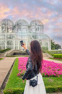 a woman taking a picture in front of a greenhouse at Hotel Moov Curitiba in Curitiba
