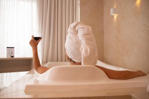 a woman sitting in a bath tub holding a glass of wine at Cancún Hotel by H Hotéis - Airport in Brasilia