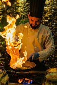 a chef cooking food in a pan on a grill with flames at Arenal Manoa Resort & Hot Springs in Fortuna