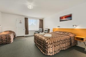 ein Hotelzimmer mit 2 Betten, einem Schreibtisch und Stühlen in der Unterkunft Arcadia Motel in Christchurch