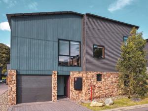 a gray house with a stone wall at Snow Stream 2 Bedroom and loft with gas fire balcony and garage parking in Thredbo