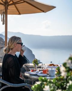 a woman sitting at a table drinking a cup of coffee at Pezoules of Oia in Oia