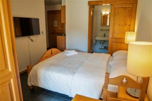 1 dormitorio con 1 cama blanca y TV en Appartement et studio, Val d'illiez, en Val dʼIlliez