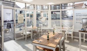 a restaurant with wooden tables and chairs and windows at Lighthouse of Stowmarket in Stowmarket