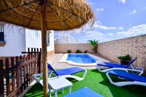 a patio with chairs and an umbrella and a swimming pool at Casa Manoli in Conil de la Frontera