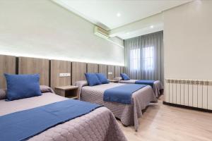 Habitación con 3 camas y almohadas azules. en Hostal María Luisa, en Madrid