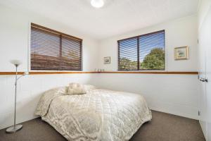 a bedroom with a bed and two windows at Kumeu Kottage in Kumeu
