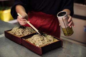 a person holding chopsticks and a box of noodles at Bunanoyado Koase in Aga