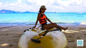 Uma mulher está sentada num ananás na praia. em The Reef Resort em Koh Kradan