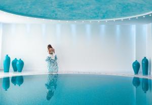 a woman standing next to a swimming pool with blue vases at Mitsis Selection Blue Domes in Kardamaina