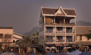 a large building with a balcony with tables and umbrellas at Indigo House Hotel in Luang Prabang