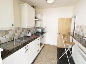 una cocina con armarios blancos y fregadero en Menai Cottage en Llanfairpwllgwyngyll