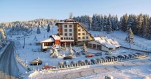 a large building in the snow with cars in front at Hotel Coop Rozhen in Pamporovo