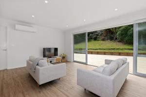 a white living room with two couches and a television at The Platinum Rendezvous - Matapouri Holiday Home in Matapouri