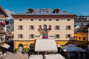 a large tan building with a black roof at Royal Hotel Cortina in Cortina dʼAmpezzo