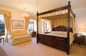 a bedroom with a canopy bed and a chair at Orton Hall Hotel & Spa in Peterborough