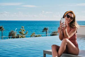 a woman sitting on a bench taking a picture of the ocean at El Llorenc Parc de la Mar - Adults Only (+16) in Palma de Mallorca