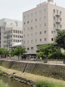 Hotel Matsumoto Yorozuya في ماتسوموتو: مبنى بجانب نهر وبه مباني في الخلف