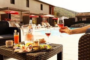 een persoon met een glas wijn op een tafel naast een zwembad bij Hôtel Les Gabarres in Tour-de-Faure