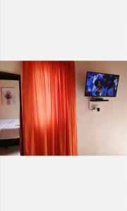a bedroom with an orange curtain and a tv on the wall at Nogixa Lodge in Umzimkulu