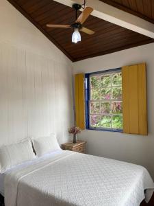Schlafzimmer mit einem Bett, einem Deckenventilator und einem Fenster in der Unterkunft Loft Largo do Ó in Tiradentes