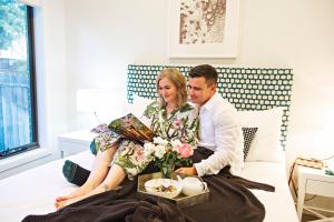 mężczyzna i kobieta siedzący na łóżku z tacą z jedzeniem w obiekcie Kirsten Accommodation Mudgee w mieście Mudgee