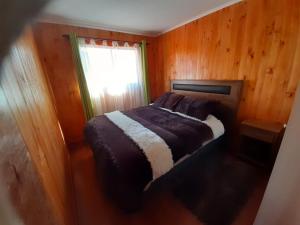 a bed in a wooden room with a window at Cabaña San Pedro in Malalcahuello