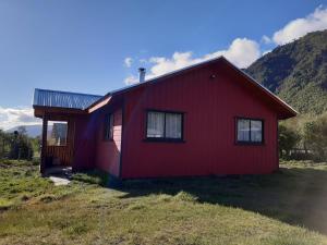 a red house in a field next to a mountain at Cabaña San Pedro in Malalcahuello