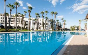 een zwembad tegenover een hotel met palmbomen bij L'Orient Palace Resort and Spa in Sousse