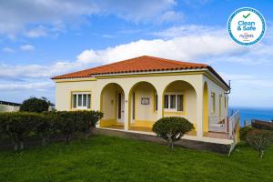 a small yellow house with the ocean in the background at Casa dos cinco sentidos in Feteira Pequena
