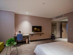 a bedroom with a bed and a desk with a tv at Vatica Wuxi Yixing City Renmin Road Hotel in Yixing