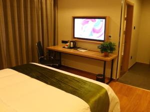 a hotel room with a bed and a desk with a television at GreenTree Inn Heze Cao County Railway Station Business Hotel in Cao