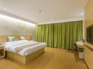 a bedroom with a bed and a desk and green curtains at GreenTree Inn Xuzhou Ou Shasha Building Materials City Express Hotel in Xuzhou