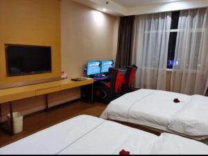 a hotel room with two beds and a desk with a television at GreenTree Inn Yulin South Changcheng Road Business Hotel in Yulin