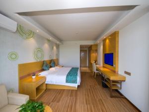 Dormitorio con cama, escritorio y TV en GreenTree Inn Qionghai Boao Railway Station Business Hotel, en Qionghai