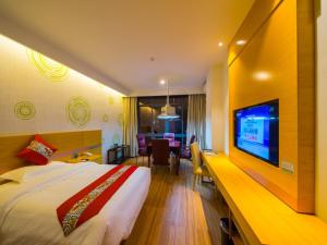 a hotel room with a bed and a flat screen tv at GreenTree Inn Qionghai Boao Railway Station Business Hotel in Qionghai