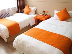Cette chambre d'hôtel comprend 2 lits avec des draps orange et blancs. dans l'établissement Shell Jining Yinzhou District Beihuan Road Innovation Building Hotel, à Jining