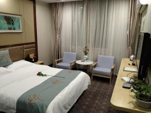 ein Hotelzimmer mit einem Bett, 2 Stühlen und einem Tisch in der Unterkunft GreenTree Alliance Xinyang Pingqiao District Nanjing Road Dongyang Hotel in Xinyang