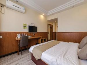 Schlafzimmer mit einem Bett, einem Schreibtisch und einem TV in der Unterkunft Shell Kaifeng City Lancao County Women and Children Hospital Hotel in Kaifeng