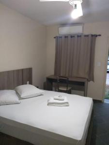 a bedroom with a white bed with a desk and a window at Hotel Pousada Jaguariuna in Jaguariúna