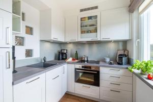 una cocina blanca con armarios blancos y fregadero en Appartement-Leuchtturmblick, en Hörnum