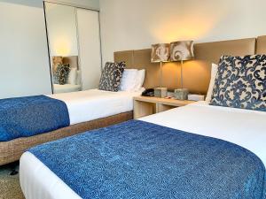 a hotel room with two beds and a mirror at Ramada Suites by Wyndham Albany in Auckland