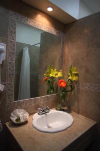 
a bathroom with a sink, mirror, and flowers in it at Hotel CasAntica in Oaxaca City
