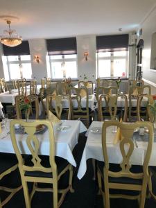uma sala de jantar com mesas e cadeiras brancas e janelas em Värdshuset Hwitan em Falkenberg