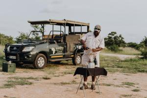 un uomo in piedi accanto a un tavolo di fronte a un veicolo di Nkambeni Safari Camp a Hazyview